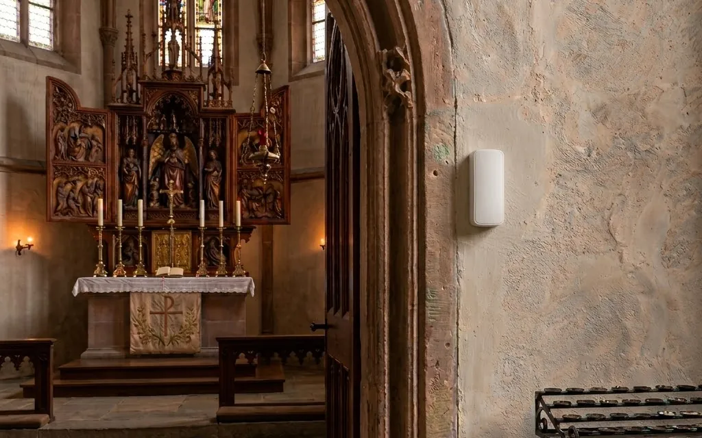 RoomAlyzer Air Mini+ sensor mounted on a stone wall in a church, discreet wireless climate monitoring